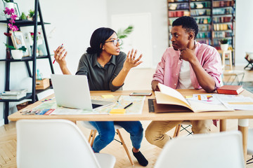 African American marriage discussing interesting ideas while creating project remotely sitting at home desk with modern laptop computer,youthful couple cooperating during distance job in home interior