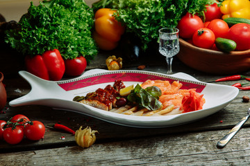 Restaurant dish with vegetable decor on a wooden background. Set of salted fish cut into slices on a plate.