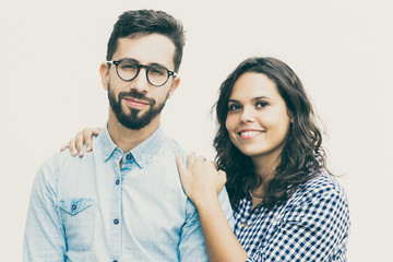 Positive Latin woman hugging male friend, couple smiling at camera. Young woman in casual and man in glasses standing isolated over white background. Couple or friendship concept