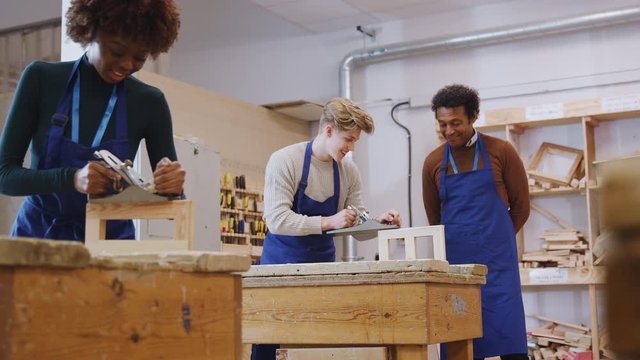 Male tutor with carpentry student in workshop studying for apprenticeship at college using wood plane - shot in slow motion