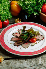 Restaurant dish with vegetable decor on a wooden background. Beef cut-up on a plate with greens.