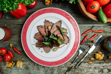 Restaurant dish with vegetable decor on a wooden background. Beef cut-up on a plate with greens.