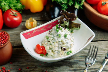 Restaurant dish with vegetable decor on a wooden background. Russian salad Olivier on a plate with herbs.