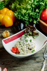 Restaurant dish with vegetable decor on a wooden background. Russian salad Olivier on a plate with herbs.