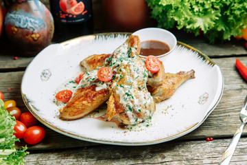 Restaurant dish with vegetable decor on a wooden background. Tobacco chicken with sauce and herbs on a plate.