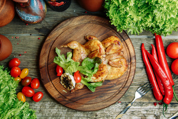 Restaurant dish with vegetable decor on a wooden background. Tobacco chicken with sauce and herbs on a plate.