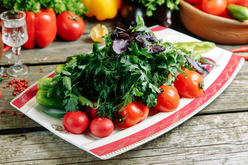 Azerbaijani restaurant dish with vegetable decor on a wooden background. Sliced vegetables and herbs on a plate.