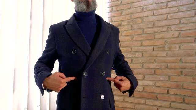 elegant man dressed in a blue three-quarter coat buttons the button and shows it to us