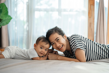 happy asian mother playing together with her baby on the bed