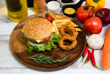 Homemade fresh tasty hamburger side dish with tomato, french fries, ketchub, mastard, salt and pepper on wood plate with white wooden plank background