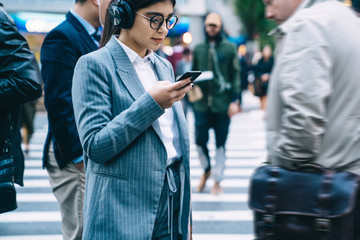 Concentrated female in headphones browsing smartphone on street