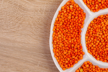 Orange lentils. Background texture of grains of orange lentils. Top view of dry lentils in a white plate. Close-up, horizontal, place for text. The concept of a healthy diet and agriculture.