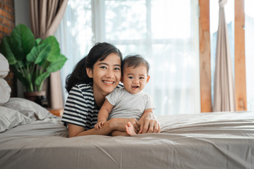 Fototapeta premium happy asian mother playing together with her baby on the bed
