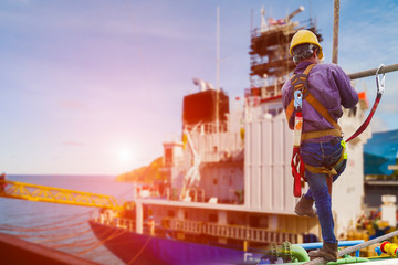 Worker in shipyard wearing safety harness with staging on accommodation background.