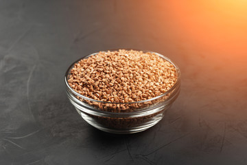 Buckwheat in a glass plate on a black background in the sunlight.