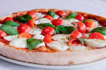 italian pizza margherita with tomato and basil on a white table