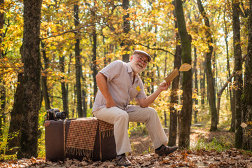 Fototapeta premium Hobby and leisure. Grandfather with vintage suitcase in nature. United with nature. Weekend in nature. Vacation and relax. Retirement concept. Elderly people. Mature man with white beard in forest