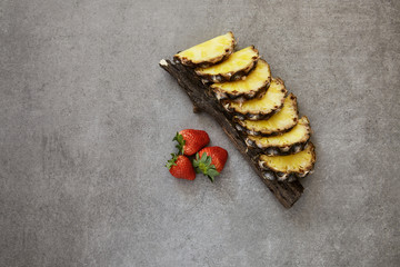 
Slices of juicy ripe pineapple on a eucalyptus branch and red sweet strawberries. Gray stone background.