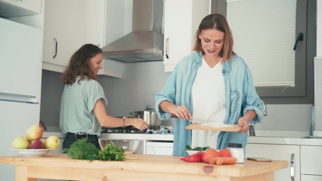 Two young pretty caucasian women cooking in the bright kitchen. Friends are having fun while cooking together.