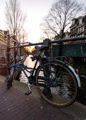 Fototapeta na wymiar A bicycle next to a water channel in Amsterdam, with a church on the background under the sunset