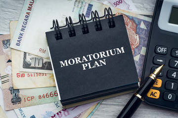MORATORIUM PLAN text with fountain pen, calculator, currency banknotes and notepad on wooden...