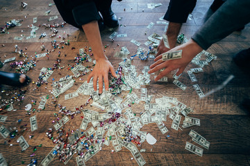 Several pairs of hands pick up dollar bills from the floor