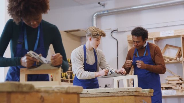 Male tutor with carpentry student in workshop studying for apprenticeship at college using wood plane - shot in slow motion