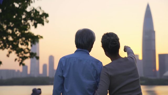 rear view of asian senior couple looking at sunset on city skyline by a river