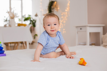 Happy toddler in blue bodysuit sits at home on bed playing with developing toys