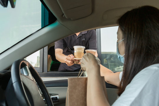 Woman in protective mask taking coffee at drive thru during covid-19 outbreak.