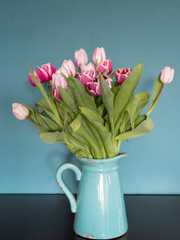 Fresh pink and red tulip flowers bouquet on shelf in front of green wall. View with copy space