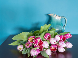 Fresh pink tulip flowers bouquet on a old brown table in front of a green wall. View with copy space and shadow