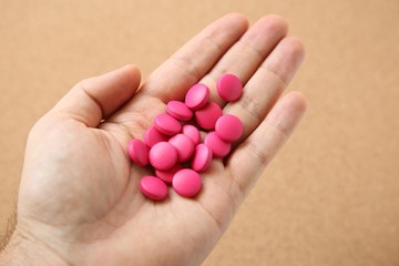 Hand holding pink pills (medical prescription medication). 