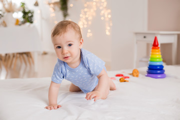 Happy toddler in blue bodysuit sits at home on bed playing with developing toys
