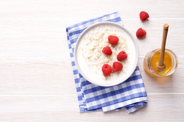 Oatmeal porridge with fresh raspberries in bowl on white wooden table. Healthy breakfast