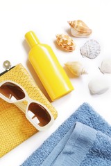 Yellow cosmetic bag, sunscreen bottle, sunglasses, blue towel and seashells. Summer beach essentials. Travel photo
