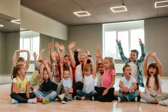 Happy dancers. Group of positive little boys and girls in fashionable clothes posing with their young female teacher in the dance studio