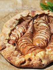 Homemade seasonal French pear cookies - galette with ripe pears, cardamom and honey. A baked galette with pears and spices on a paper lining. Close-up, mint and a jar with honey nearby.