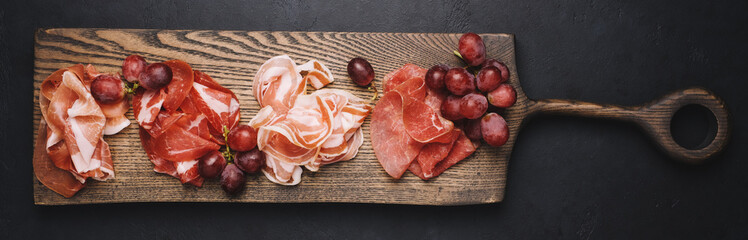 Assorted Italian meat appetizers for wine. Bresaola, prosciutto, pork neck and grapes