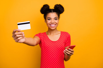 Naklejka premium Easy banking transferring. Positive afro american girl hipster hold plastic card cell phone recommend pay online modern technology wear red dotted t-shirt isolated bright shine color background