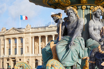 Place de la Concorde fountain statues with golden details and building with french flag in a sunny...