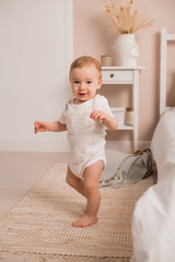 Fototapeta premium Cute toddler learns to walk the bed window at home.First steps of baby boy learning to walk in white sunny bedroom.Nursery interior