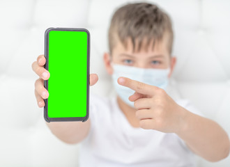 Boy wearing medical mask points on  empty screen of a smartphone