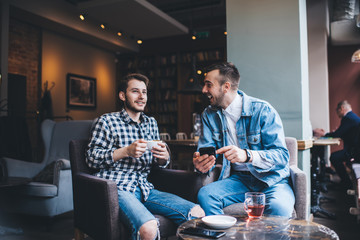 Smiling men using smartphone in modern cafe and talking