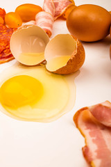 Broken chicken egg, slices of bacon and sausage and tomatoes on a white background. Close up.