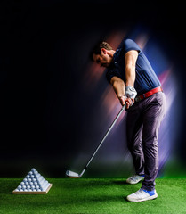 Golf player practicing in a driving range with pyramid of golf balls  