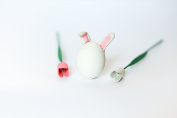horisontal shot of an easter bunny made from egg with ears attached on white background between wooden tulips, fresh spring minimalism