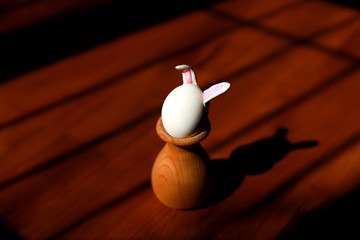 horisontal shot of an easter bunny made from egg with ears attached in a wooden holder on dark background between gates made from sunshade, self isolation concept