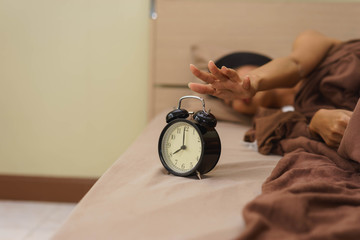 Asian woman is reaching to alarm clock.