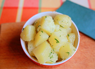 boiled potatoes with herbs in a red plate on a wooden stand, close-up, proper nutrition